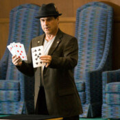 Marty G wearing fedora performing magic trick on stage involving four very oversize playing cards.