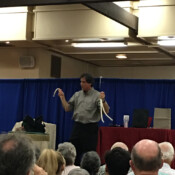 Marty G in front of seated audience performing magic trick.