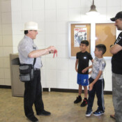 Marty G wearing white hat performs magic trick for two grinning boys and their smiling father.